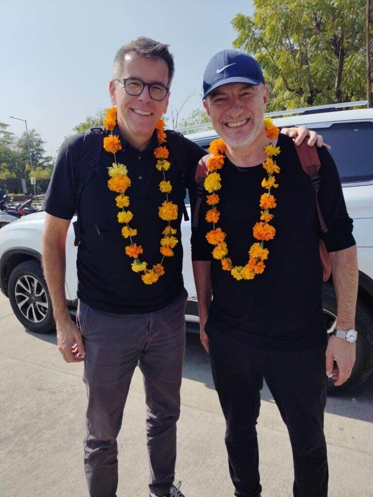 Two guests wearing marigold garlands beside their private vehicle on arrival