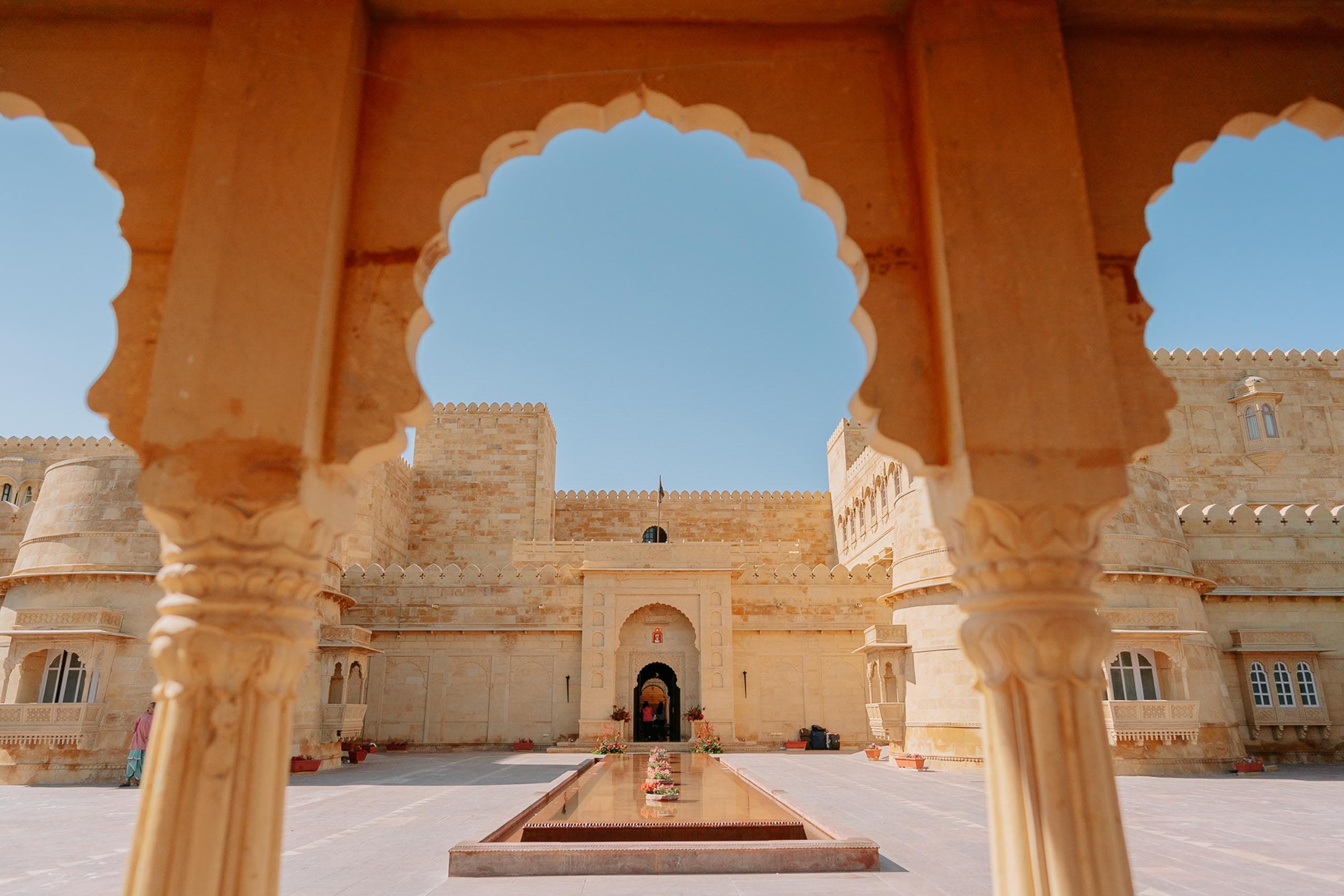 Suryagarh Jaisalmer's carved sandstone entrance courtyard, framed by a scalloped chattri arch, with the fort-style facade beyond
