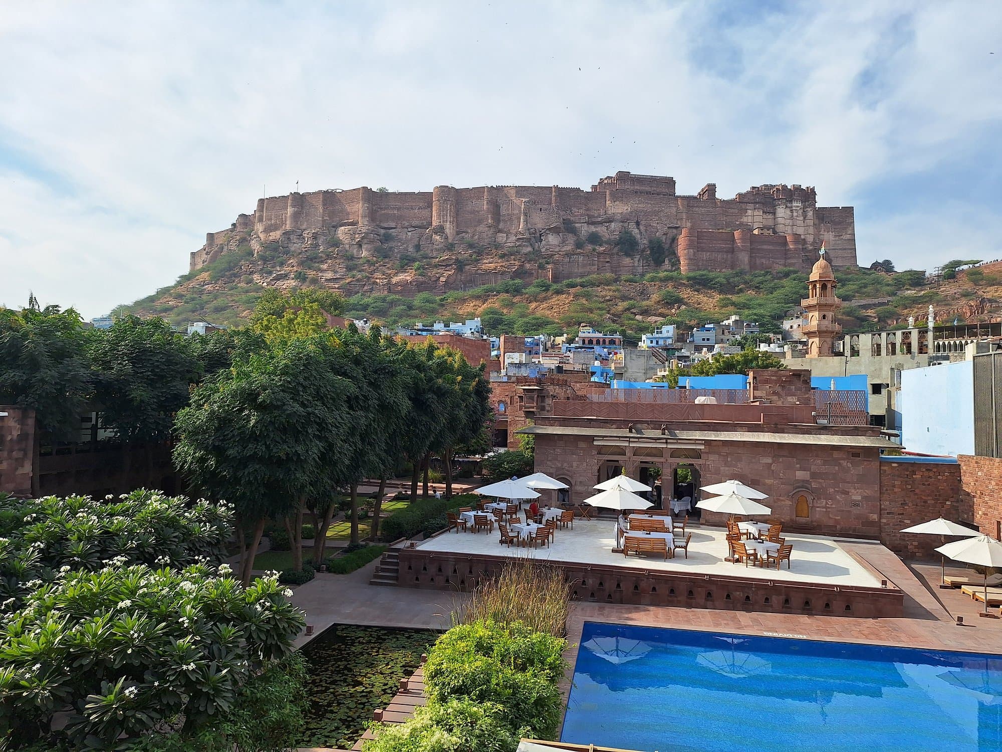RAAS Jodhpur's rooftop pool and dining terrace by day, with Mehrangarh Fort towering directly above the property