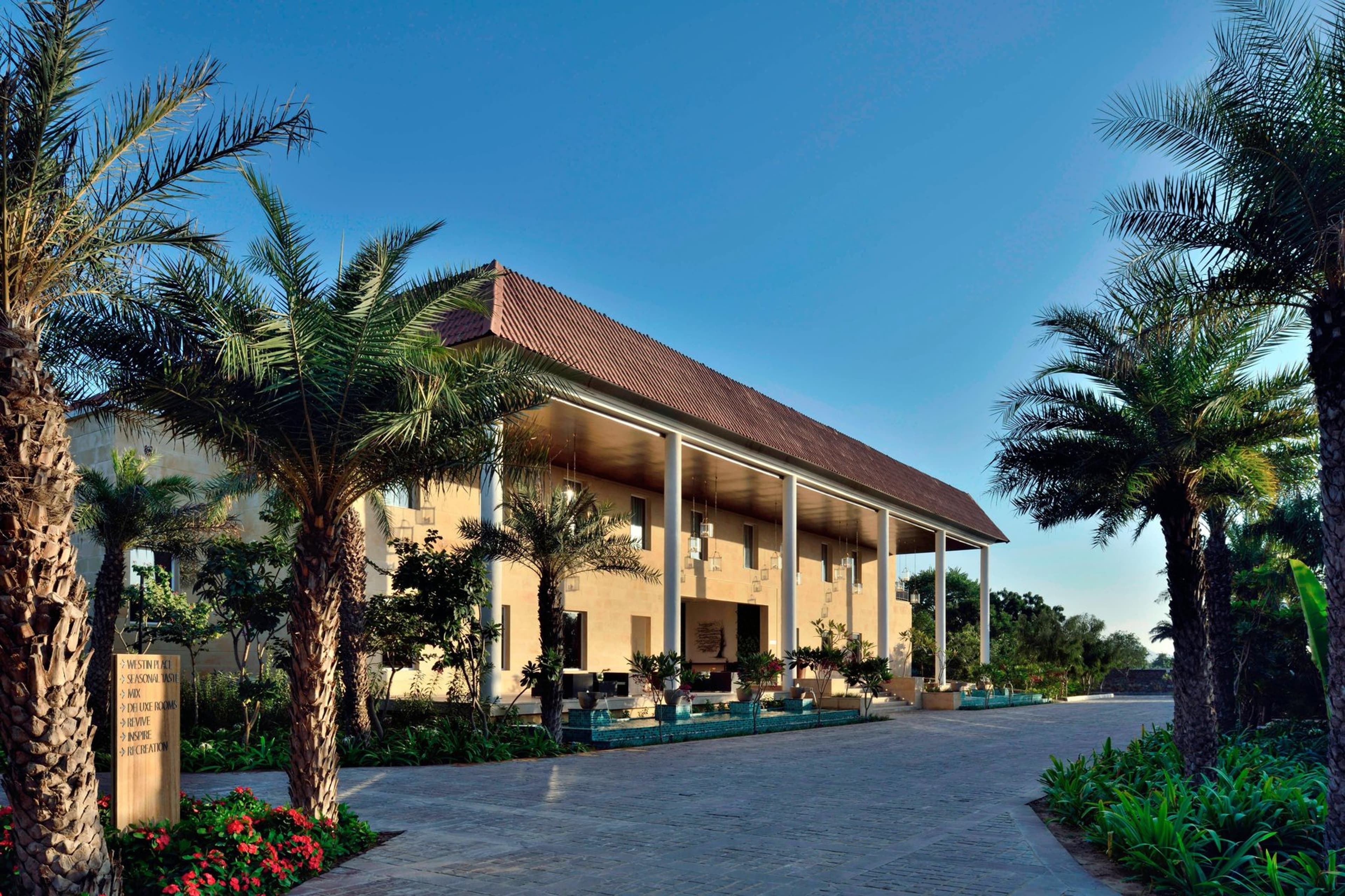 The Westin Pushkar Resort & Spa's palm-lined entrance and covered porte-cochere at sunrise, with a Westin signpost