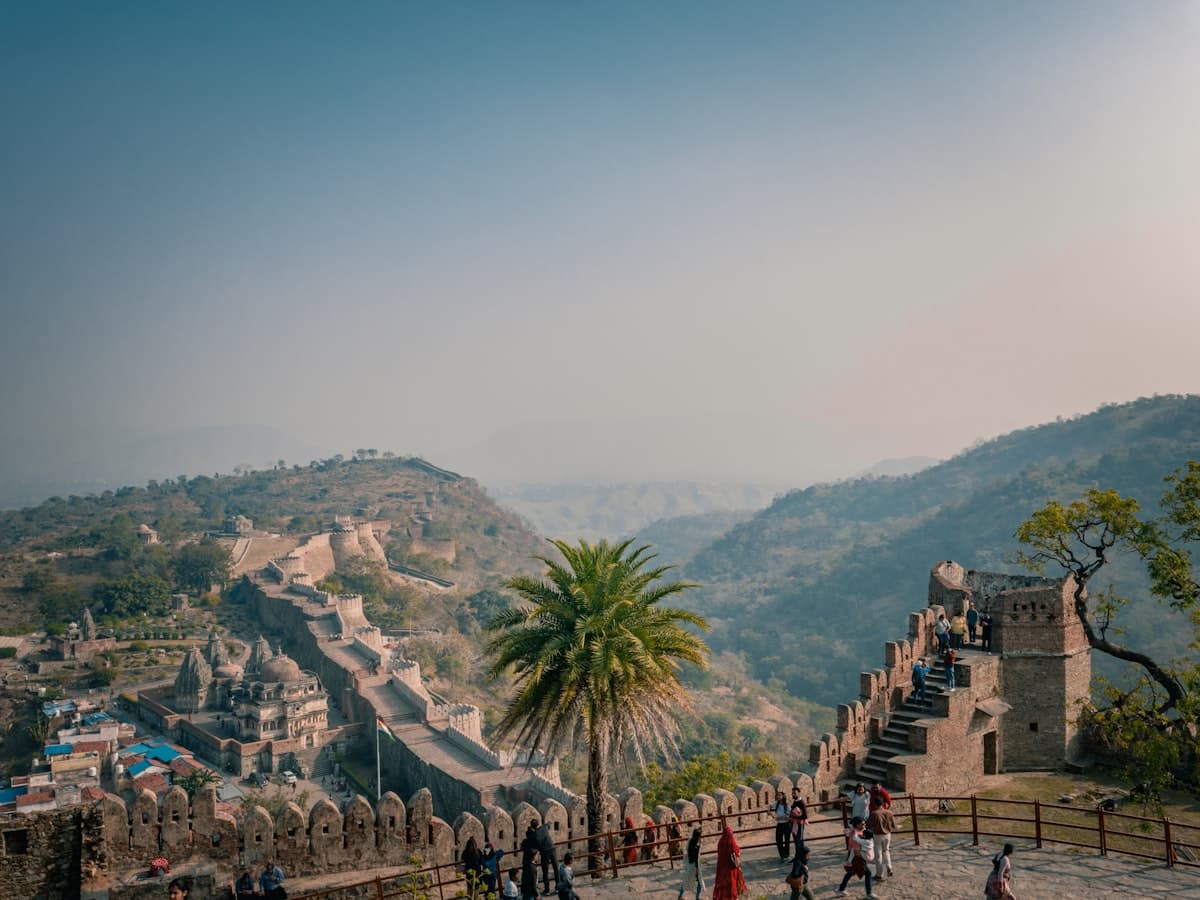 Visitors walking Kumbhalgarh Fort's ramparts with the fortress wall stretching across the hills behind