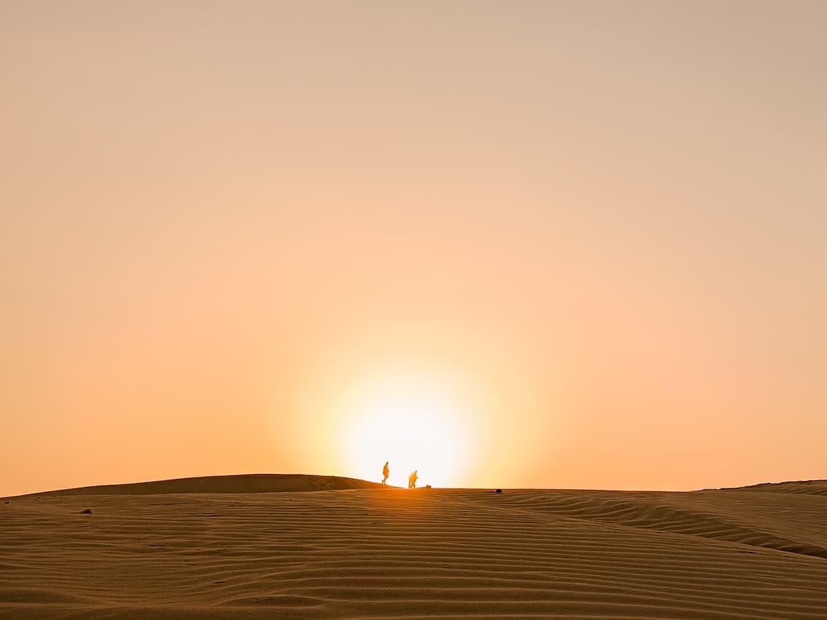 Two figures silhouetted on the Thar Desert's rippled dunes at sunset
