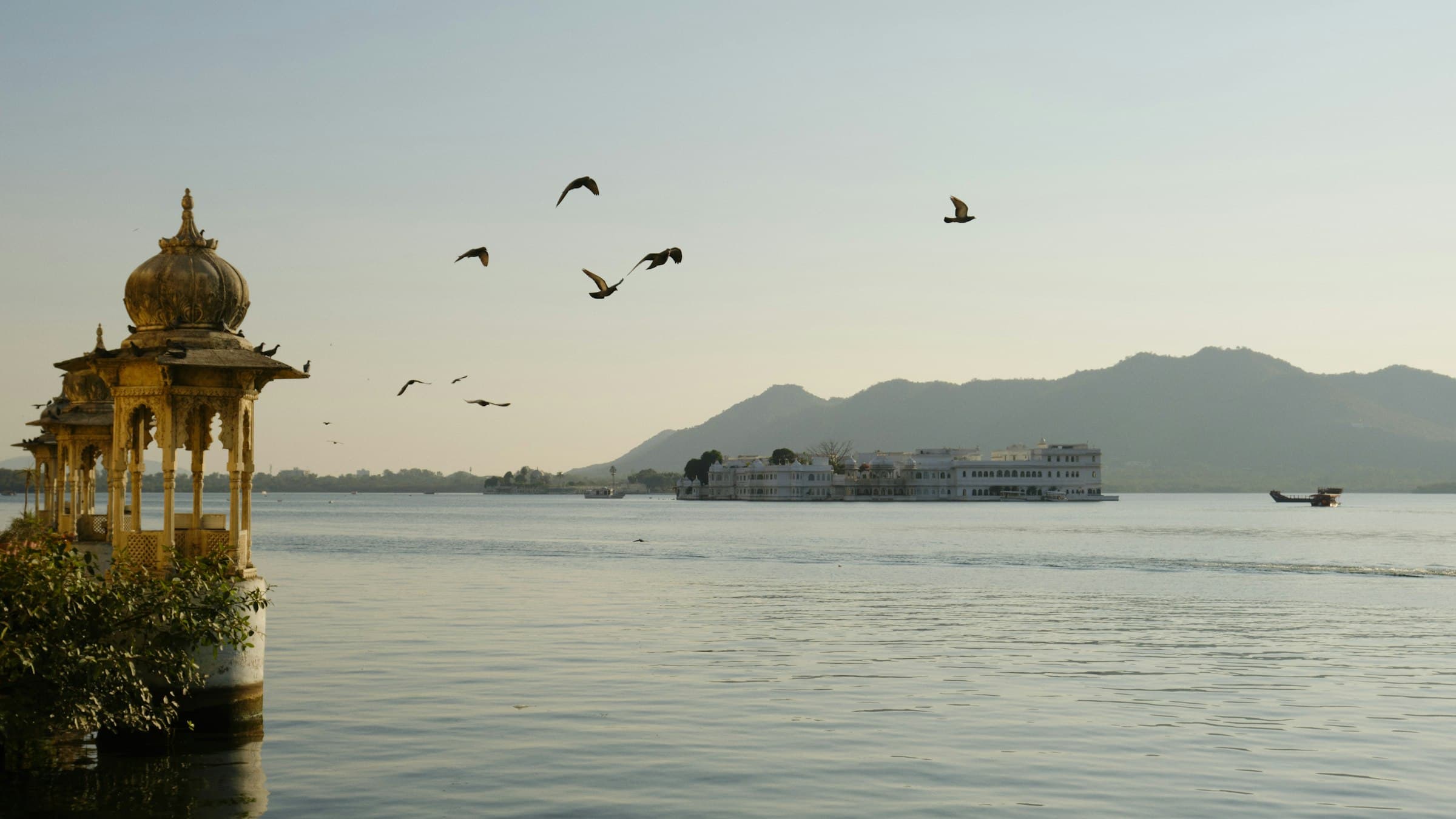 Taj Lake Palace and Lake Pichola at Udaipur with birds in flight overhead, showcasing the city's romantic lakeside beauty