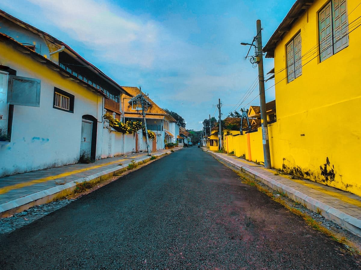 A quiet Fort Kochi street lined with yellow colonial buildings under a clear blue sky