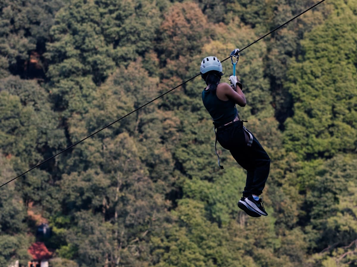 A person riding a zip line over green forest